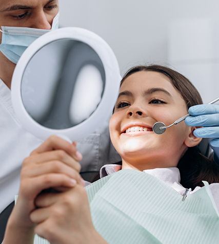 Girl in dental chair looking at her smile in a mirror