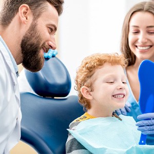 Child smiling as dentist shows him his teeth with a mirror