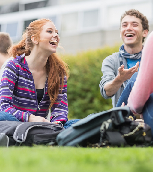Circle of teens sitting in a circle on grass and laughing