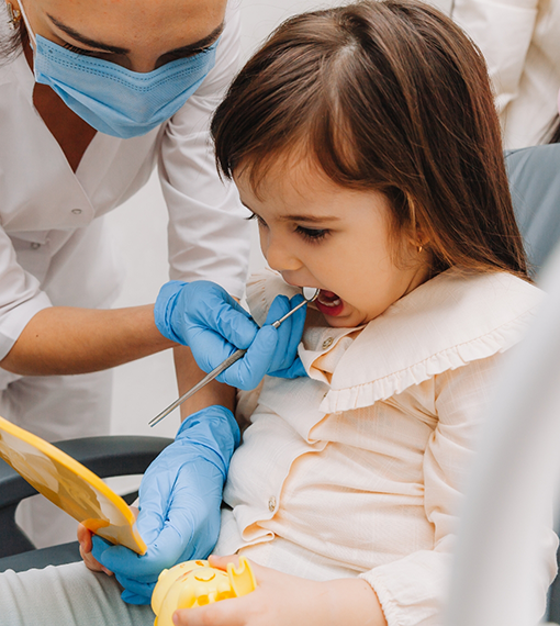 Toddler looking at her mouth in a mirror while receiving a dental exam