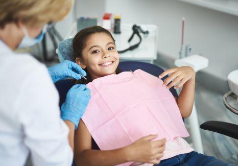 Young girl in dental chair with light pink dental bib