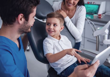 Dentist showing a tablet to a young boy in the dental chair