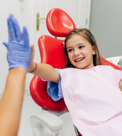 Young girl in dental chair giving a high five to her dentist