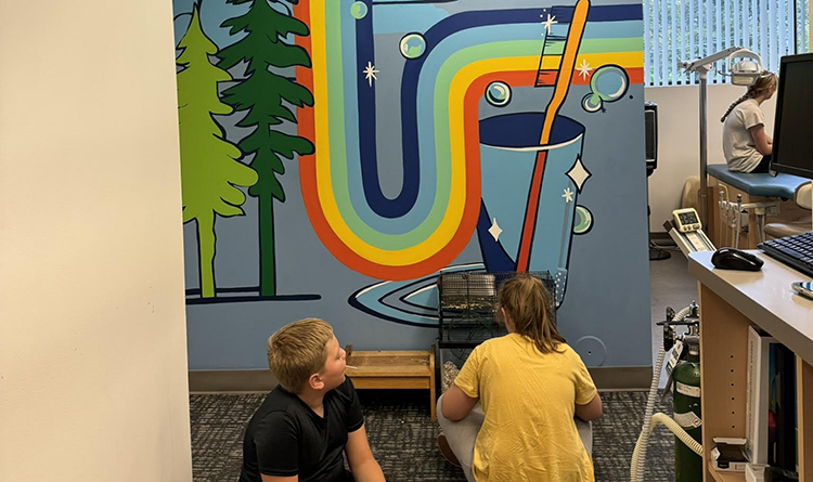 Two kids sitting on carpeted floor in dental office