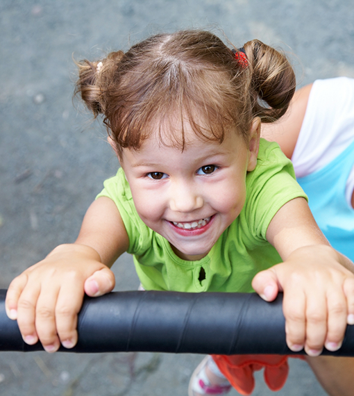 Smiling girl hanging from a bar on a playground after pediatric dental services in Portland