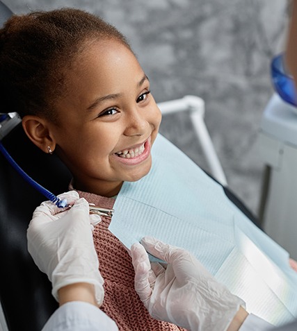 Child in treatment chair smiling at dentist