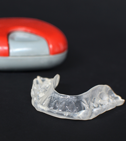 Clear mouthguard next to a red plastic case