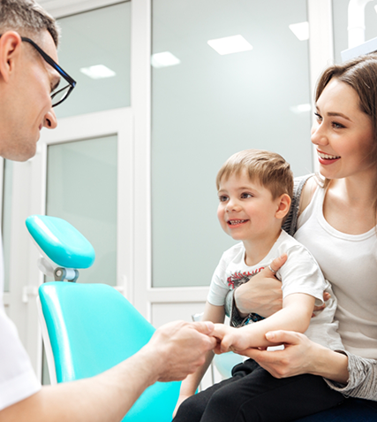 Toddler boy shaking hands with dentist while sitting on his mothers lap
