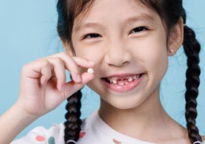 Child with missing front teeth holding up extracted tooth.
